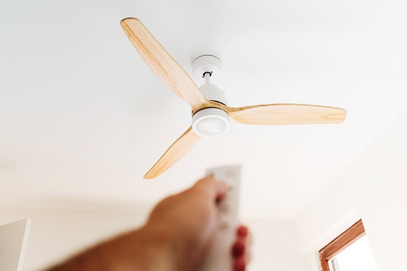 How to Choose the Right Ceiling Fan. Photo of a person adjusting a fan with a remote.